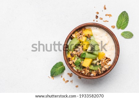 Mango yogurt with granola and kiwi in wooden bowl on white background. Healthy dairy product breakfast 