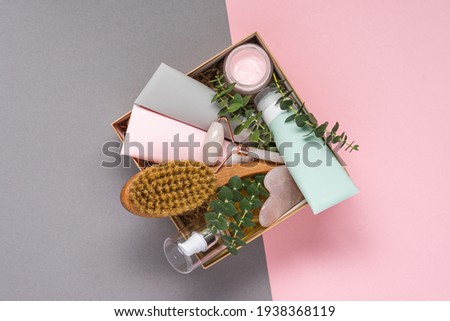 Beauty box with face and body care products on pink and grey background. Tubes with cream and lotion, hydrophilic oil, facial roller, guache massager, body brush. Natural cosmetics gift Foto stock © 