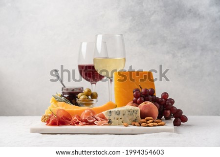 Assorted cheese, ham, fruit, jam, bread sticks, nuts. Cheese platter. Marble tray on table covered with linen tablecloth. Side view 