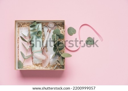 Beauty box with face and body care products on pink background. Tubes with cream and lotion, , facial roller, guache massager, eucalyptus leaves. Organic cosmetics gift Foto stock © 