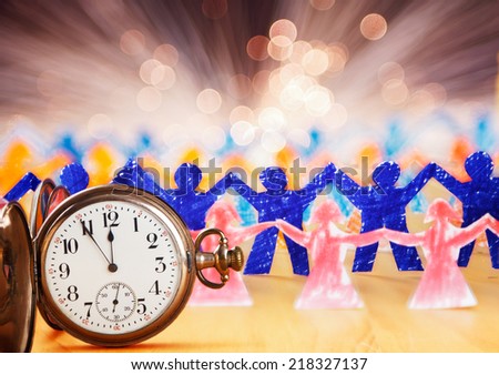 Improvisation of celebration New Year with paper people dancing, and old pocket watch in the front.