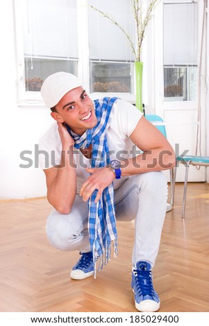 smiling handsome fashion man with a scarf and white cap posing in the living room