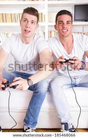 two modern guys on sofa playing computer game holding controllers