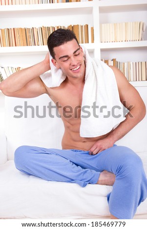 handsome guy with naked torso wearing pajamas and towel around neck relaxing on couch