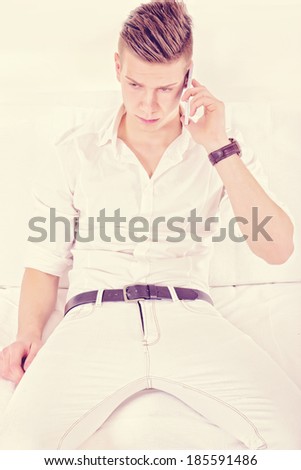 modern fashion guy in white talking on the phone sitting on sofa in vintage style