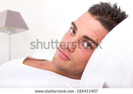 handsome sensual man lying in bed. Closeup face with seductive beautiful eyes looking at camera holding head on the pillow