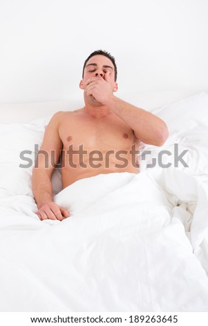 sleepy handsome tired man yawning in bed at home waking up