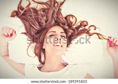 View from above of a beautiful woman looking at camera on bed with her long hair spread out. Vintage retro effect style