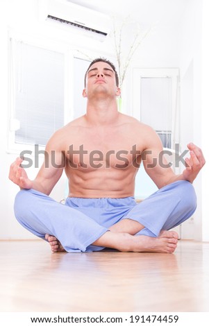 young handsome muscular  half naked man doing yoga and meditating indoors in living room, domestic atmosphere