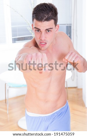 shirtless man exercising fight and punch at home, muscular man raising fists towards camera