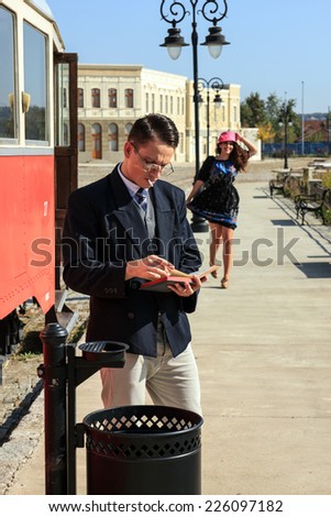 Romantic scene with man by the train reading book and retro woman running towards him on train station