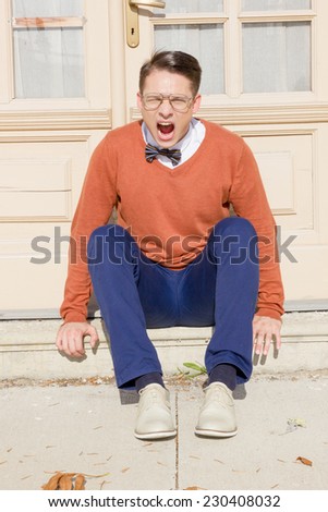 angry  man with open mouth with glasses and sweater sitting on steps in front of house and posing  while looking at camera, vintage retro fashion  photo