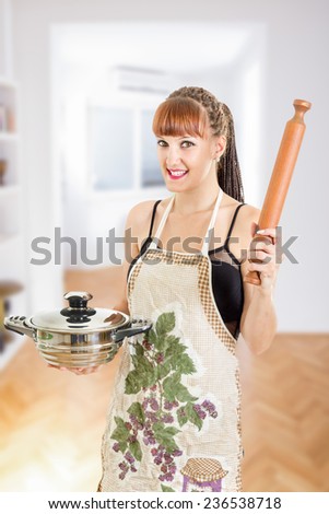 Beautiful young woman in the kitchen wearing apron holding pot and rolling pin smiling , Cooking concept , Sexy housewife in the kitchen