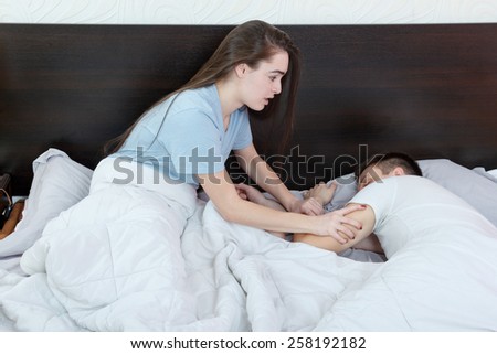Woman  wakes up man who is late for work, delays due to fatigue. Wear of marriage. Couple was asleep in bed. Impatience woman wakes up tired husband.