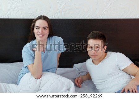Young cute caucasian couple, man and woman in bed smiling and looking at camera. Domestic morning atmosphere