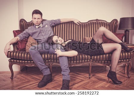 Elegant  young couple in love lying and sitting on a vintage couch or two-seater. Glamour man and woman in luxury room. Vintage retro photo. Fashion style