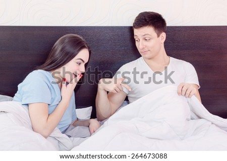Handsome satisfied man sure in himself showing under cover in bedroom strong penis erection to pretty surprised woman. Sexy young couple in morning, domestic atmosphere. Photo of healthy male potency.
