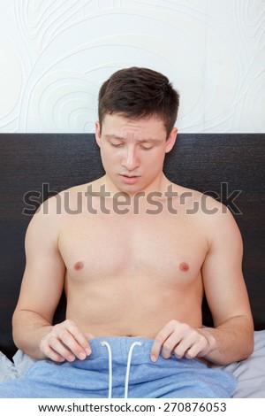 Young man in bed having problems with potency looking at his penis under pants , Worried rejected man having trouble with erection failure