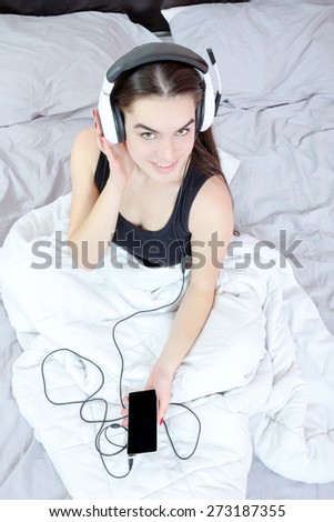 Portrait  of beautiful woman in morning or evening in night  listening sweet romantic music lying or sitting on bed at home. Young girl in pjamas with mp3 player or mobile and headphones enjoying.
