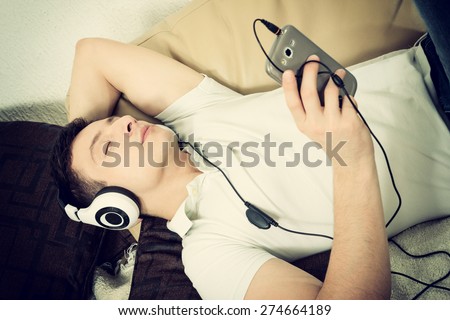 Man on couch holding smartphone listening to music with headset daydreaming