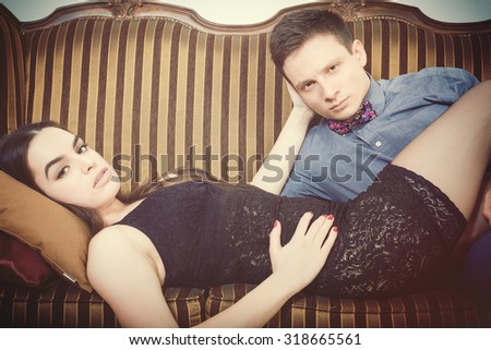 Retro vintage couple lying on the retro furniture. Young man and woman In sexy edition looking seductively at camera or at you. Vintage male and female model on sofa at home.