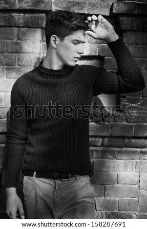 Fashion portrait of young man in black sweater poses over wall