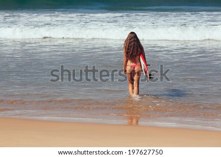 Rear view of beautiful sexy young woman surfer girl in bikini with white surfboard