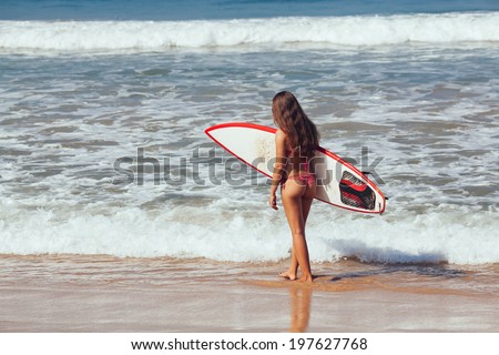 Rear view of beautiful sexy young woman surfer girl in bikini with white surfboard