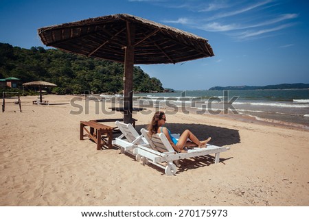 Woman on a tropical beach on deck chair under sun umbrella.woman resting under umbrella facing the seaside in a deserted beach with deep blue sky