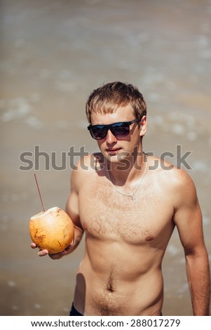 attractive man drinks coconut juice from a nut on a beach at the ocean
