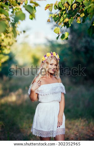 Portrait of blonde girl wearing  white dress with flower wreath in the forest . forest Nymph
