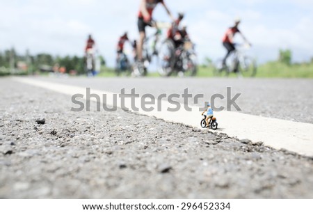 An old man  (miniature) on cycle ride in country road with a group of bicycle race background.Soft focus and shallow depth of field composition with soft pastel color.