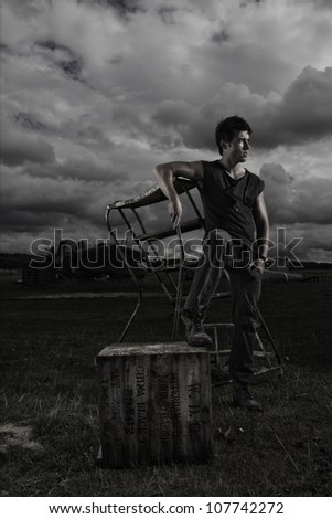 Dark stormy portrait of a casual sexy man posing on portable steps alongside an old crate outdoors under a threatening sky