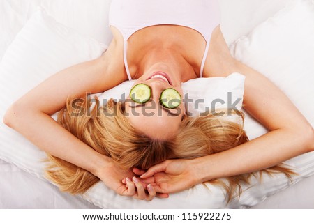 Woman reclining on her back on her bed using cucumber eyepads made of fresh sliced cucumbers to sooth her eyes