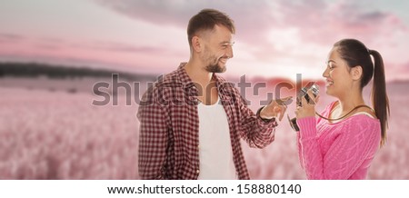 Beautiful young woman photographing her boyfriend at sunset or dawn against a pink sky as he stands pointing at the camera with a lovely smile on his face, copyspace over the surrounding countryside