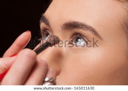 Beautician applying cosmetics on a young model using a soft brush to contour under her eyes with powder to give a smooth complexion