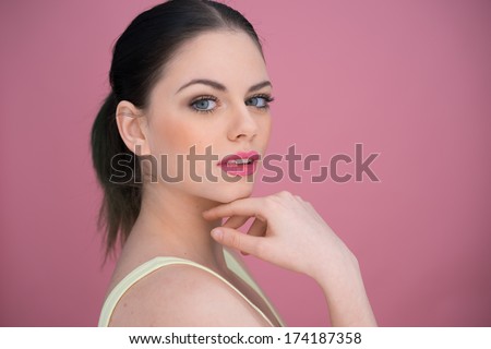 Pretty young woman with her brunette hair in a pony tail giving the camera a speculative look, over a pink background