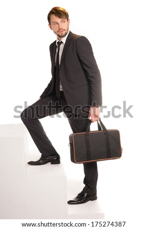 Handsome bearded stylish young businessman climbing stairs with a briefcase in his hand