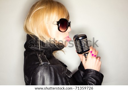 blonde woman holding a retro microphone wearing black jacket , singing rockstar