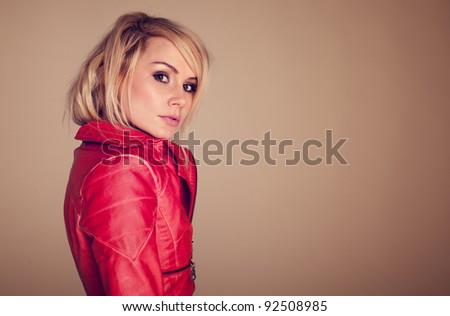 Provocative Fashionable Blonde Woman dressed in a leather jacket and glancing sideways at the camera with raised eyebrow.