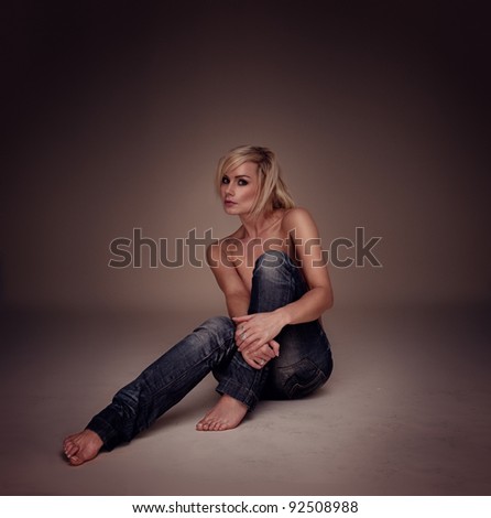 Sexy Casual Blonde Woman seated on the floor implied topless, studio portrait highligted on brown