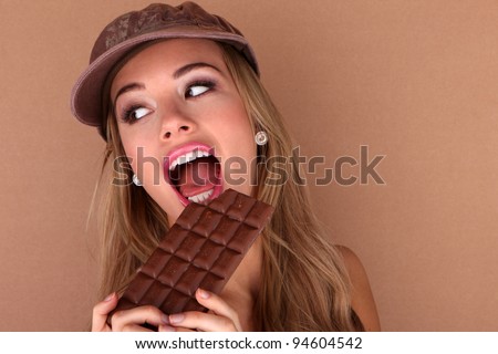 Laughing beautiful woman holding a slab of unwrapped chocolate close to her face.