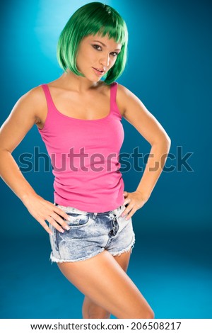 Sexy young woman with a cute modern green hairstyle posing seductively in skimpy denim shorts on a pink background