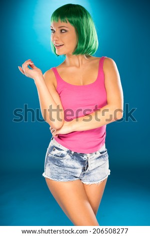 Cute slender young woman with psychedelic green hair in a matching green top, trendy sunglasses and skimpy denim shorts
