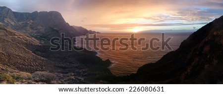 Colorful panoramic sunset or sunrise over a tranquil ocean and coastline on a cloudy day viewed from a headland or mountain peak