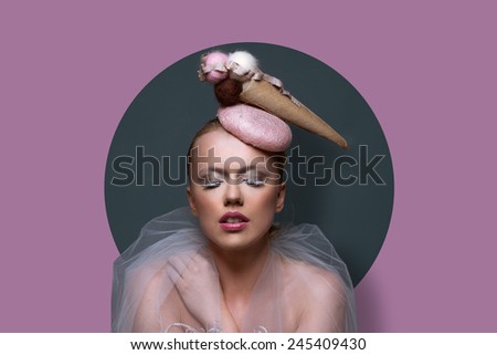 Fine art portrait of a gorgeous woman in fascinator hat in the shape of an ice cream cone with creative makeup and filmy gauze around her shoulders over a purple background