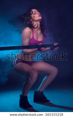 Portrait of a Sexy Athletic Young Woman Holding Fitness Bar on her Shoulders on a Dark Blue Green Background.