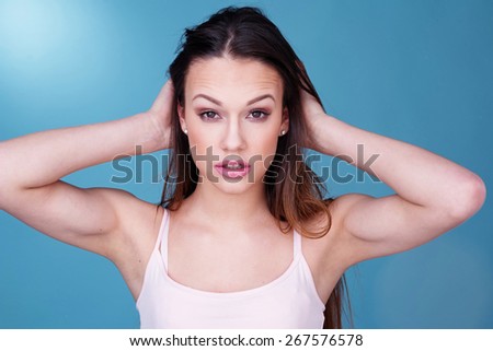 Close Up Portrait of Young Woman Wearing Tank Top with Hair in Hands Staring at Camera in front of Blue Background