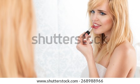 Young Smiling Blond Woman Looking Into Mirror and Applying Lipstick, Getting Ready to Go Out