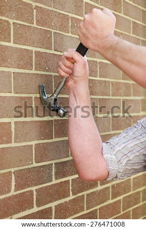 Man hitting an exterior face brick wall with a metal claw hammer in a conceptual image, close up of his hand